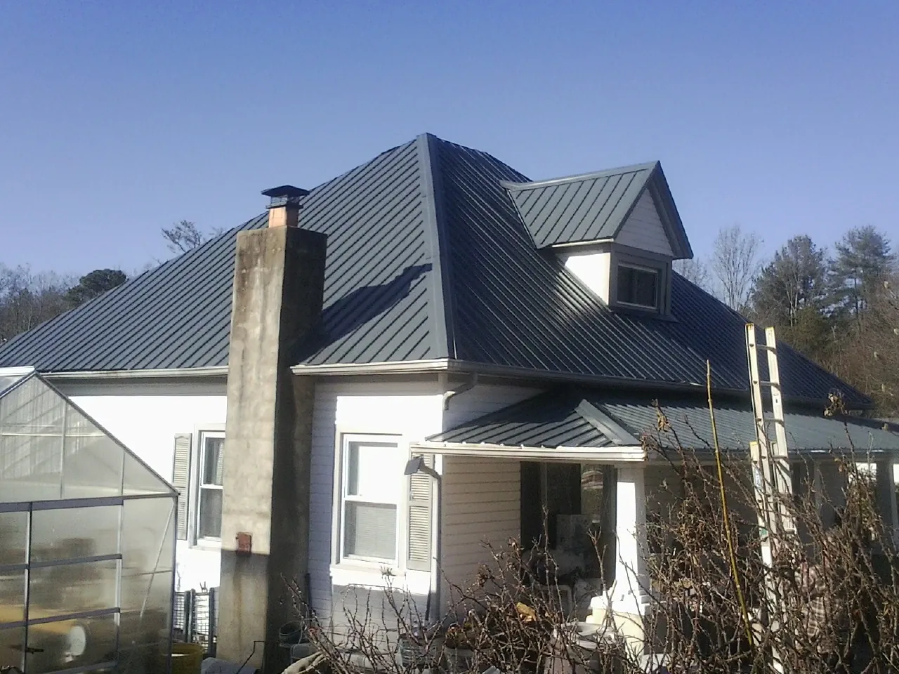 Dark blue standing seam metal roof on a white farmhouse with dormer — Slate & Tile Roof Repair by Roofing Brothers in Grassy Creek