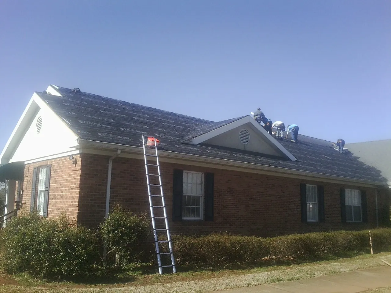 Crew tearing shingles off a brick ranch roof with a ladder set — Metal Roof Repair work by our crew in Grassy Creek