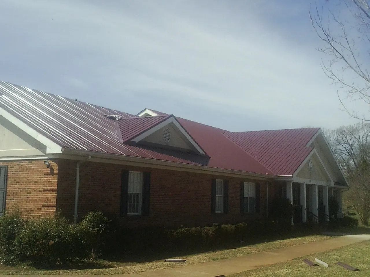 Red metal roof with gabled entries on a long brick building, from a Hail Damage Roof Repair job in Grassy Creek