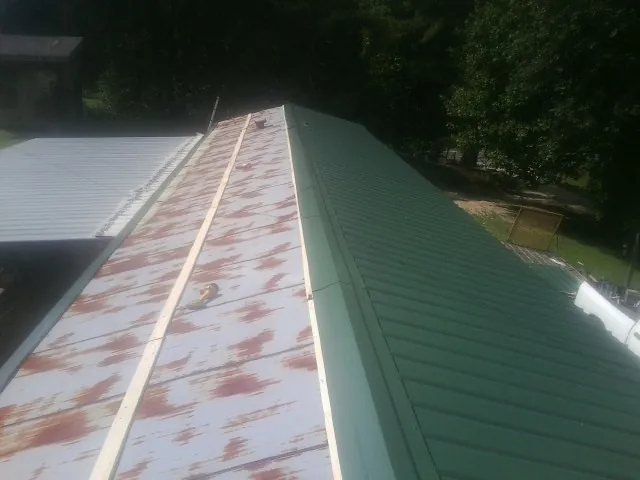 Old rusted panels beside newly installed green metal roofing — Wind Damage Roof Repair by Roofing Brothers in Grassy Creek