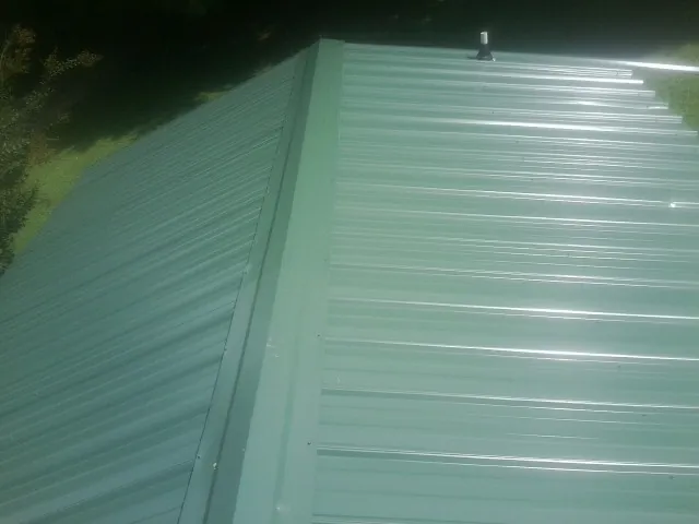 New green metal panels meeting at the ridge of a roof — Flat Roof Repair work by our crew in Grassy Creek