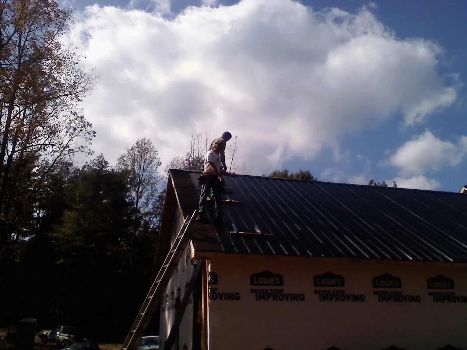 Roofer fastening dark metal panels high against a cloudy sky, from a Roof Inspection job in Grassy Creek