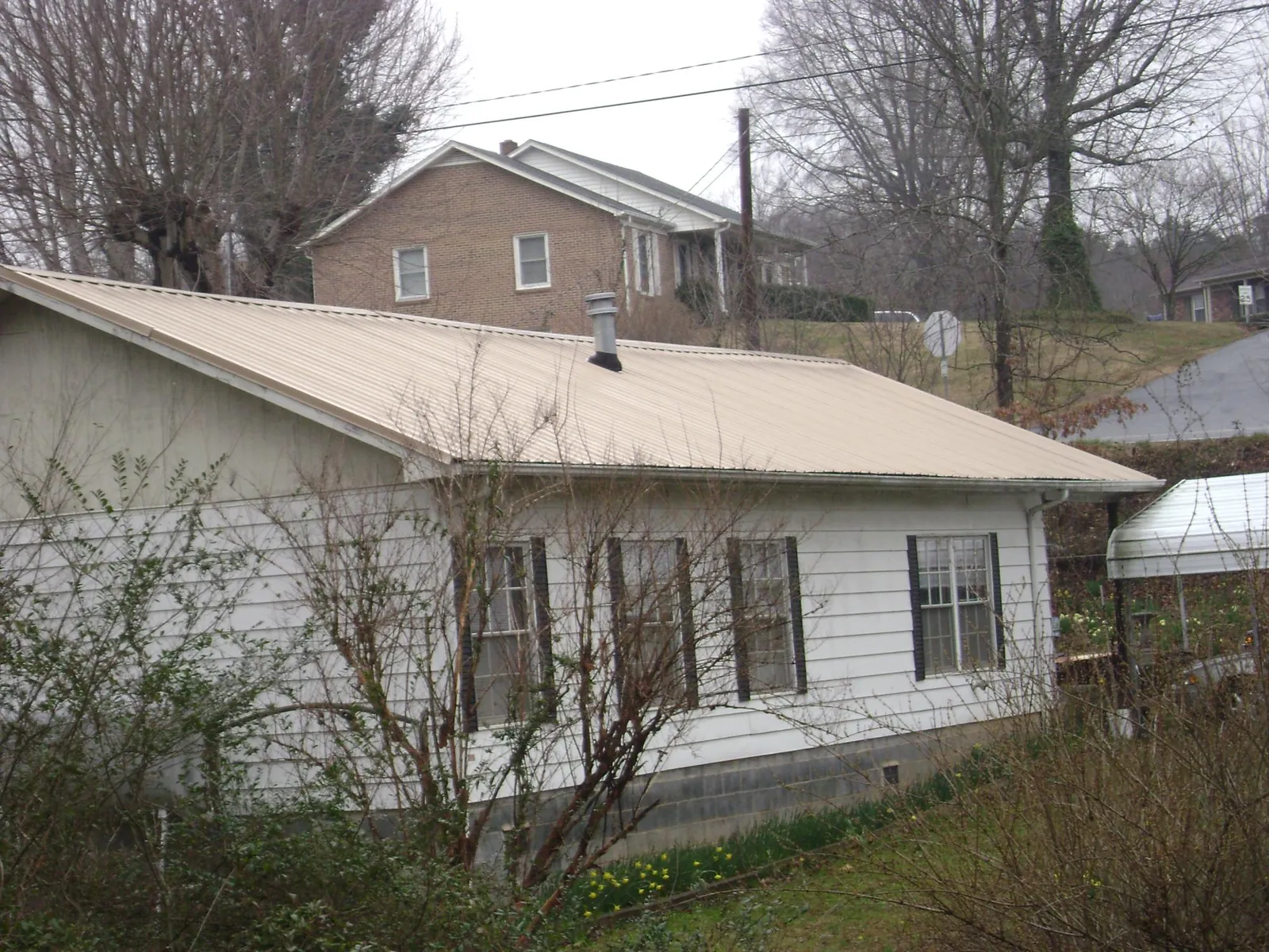 Tan metal roof on a white sided house set into a hillside — Commercial Roofing by Roofing Brothers in Grassy Creek