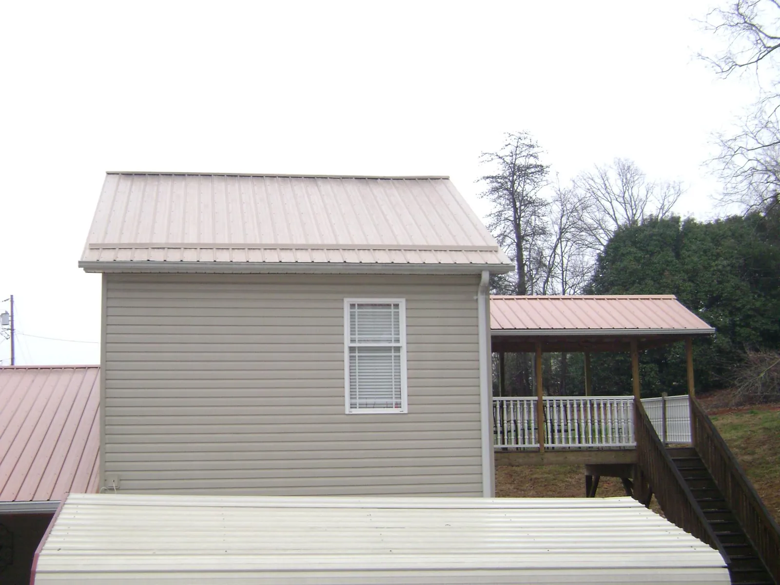 Tan metal roofs on a two story addition and attached porch, from a Roof Replacement job in Grassy Creek
